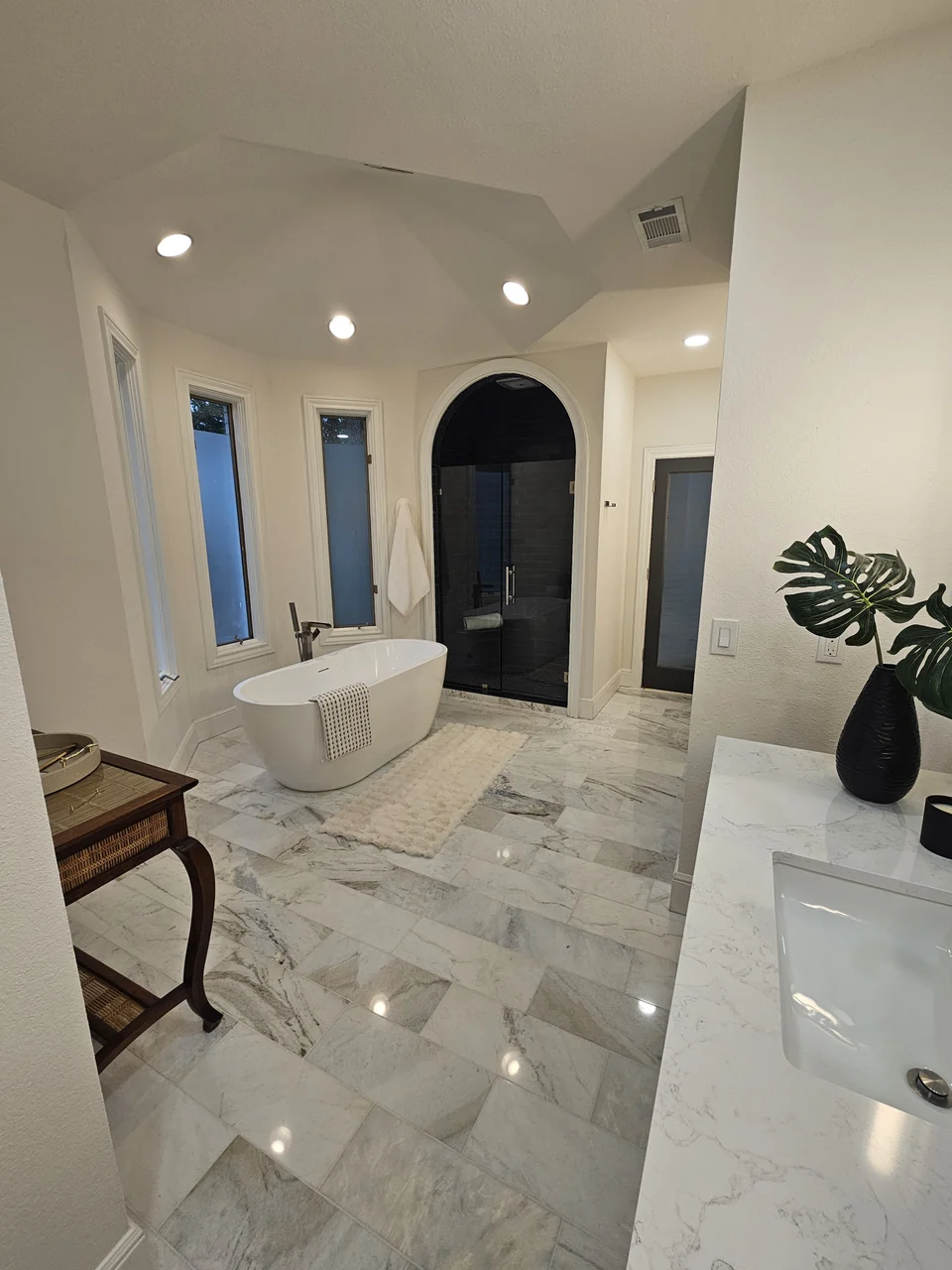 Marble-look bathroom floor beside a freestanding tub and arched shower.